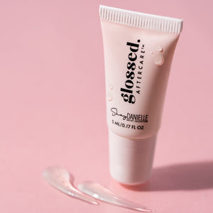 Glossed Aftercare lip balm for permanent makeup displayed on a pink background with product texture.