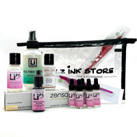 Flat lay of the Li-FT Saline Removal Starter Kit including Li-FT bottles, Non-Epi numbing solution, Tea Tree Toner, Zensa cream, and Girlz Ink Store clear travel bag, displayed on a white background for PMU artists performing safe tattoo lightening and removal.
