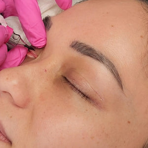 Close-up of a healed brow tattoo created with OMG® Pigments Bitchin Brown by Teryn Darling. The photo shows soft, even color retention after one session, 1.5 years healed. Artist wearing pink gloves is seen perfecting the brow shape.