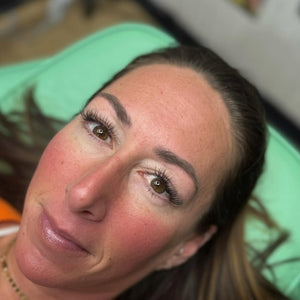 Healed brow results after one session using OMG® Pigments in Bitchin Brown and Vixen. The image shows a woman lying on a green surface with soft, natural brow color retention created by Monica @mbmpmu.